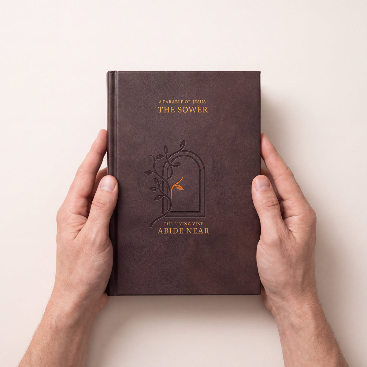 A person's hands holding a dark brown leather-bound book titled 'The Sower' against a light beige background.